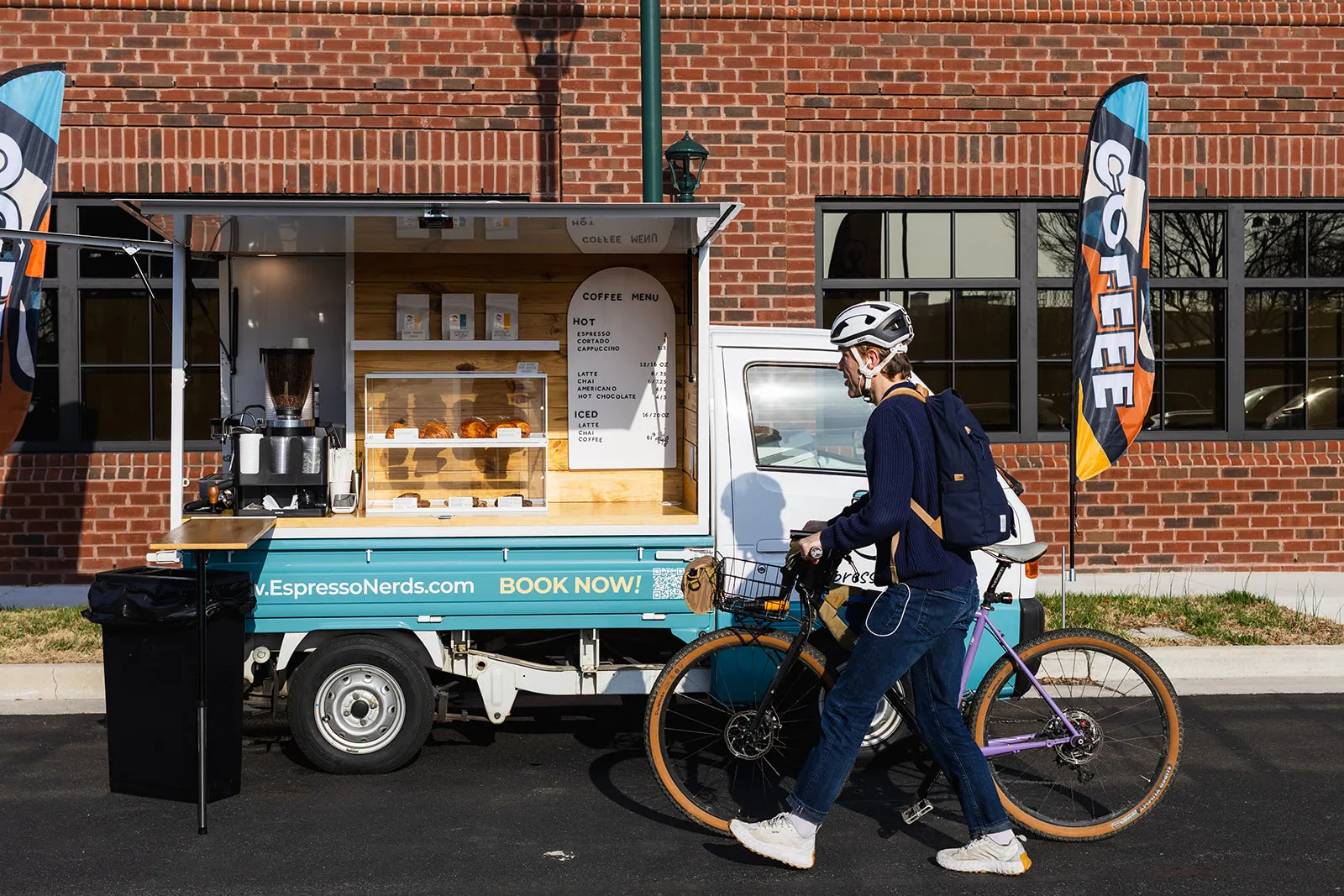 A cyclist stopping by the Espresso Nerds truck outside a brick building