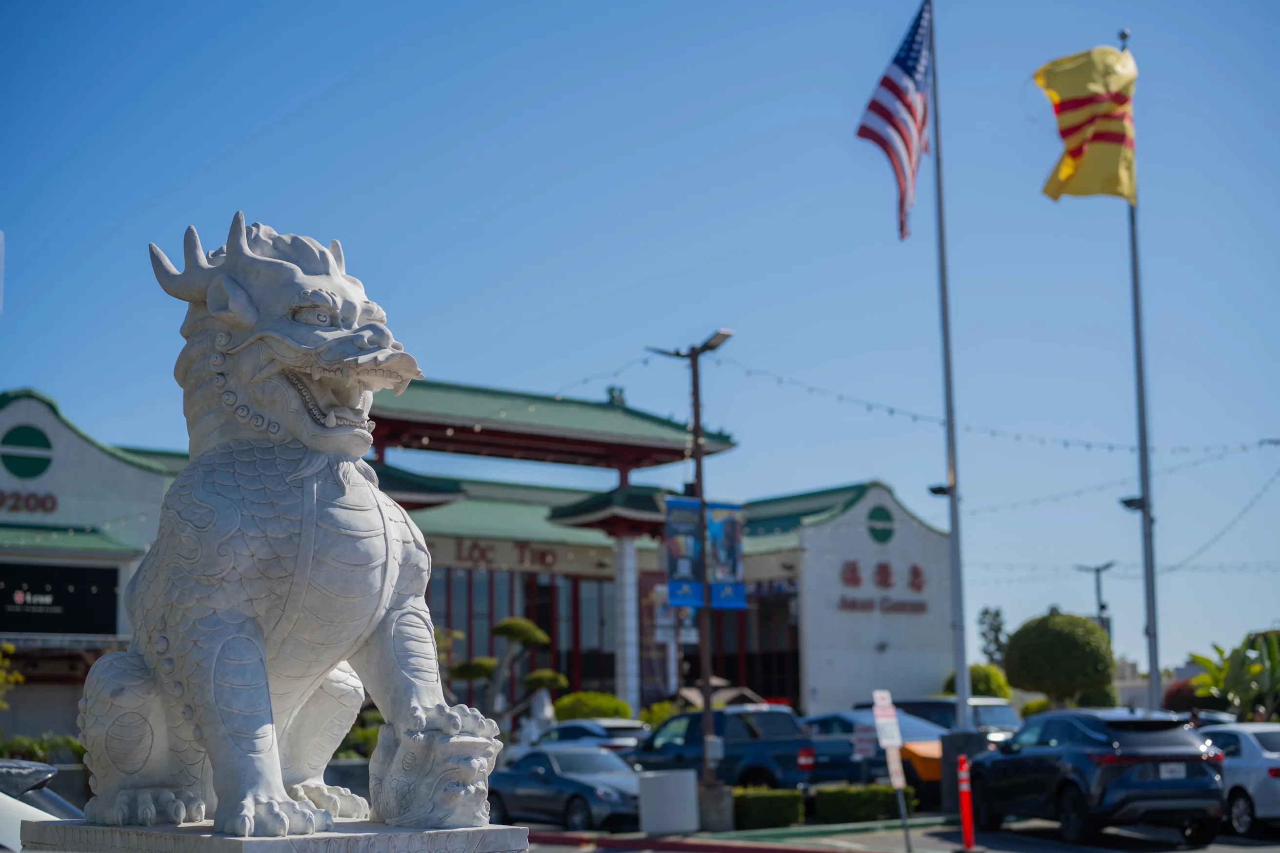 A stone guardian lion outside a Little Saigon shopping plaza in Westminster, with the Vietnamese heritage and U.S. flags flying