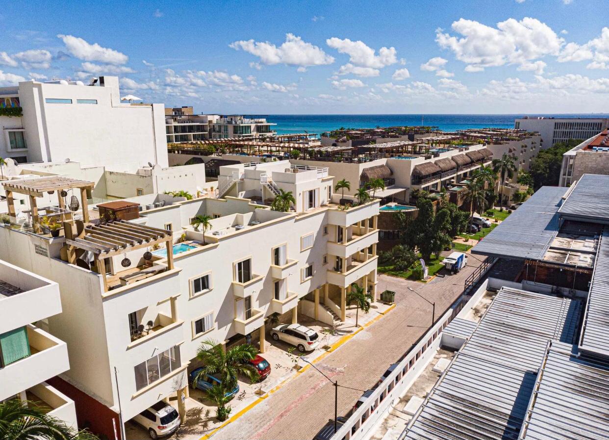 Aerial view over a residential street in Playa del Carmen, white low-rise apartment buildings with balconies and parked cars, the Caribbean beyond