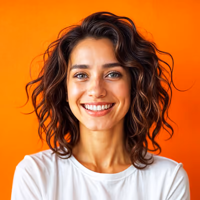 Smiling woman with curly dark hair wearing a white shirt against an orange background.