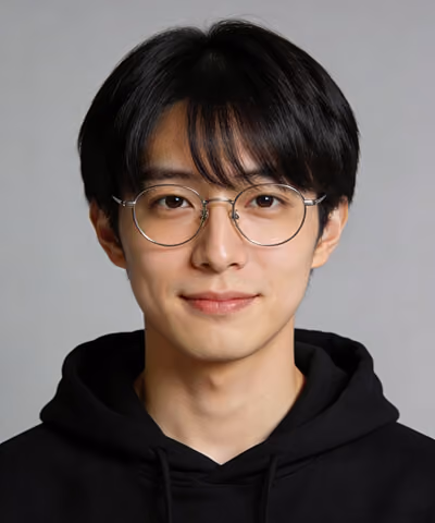 Young man with black hair wearing round glasses and a black hoodie against a gray background.