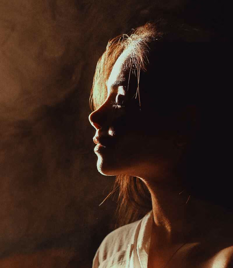 Side profile of a woman with light illuminating her face against a dark, smoky background.