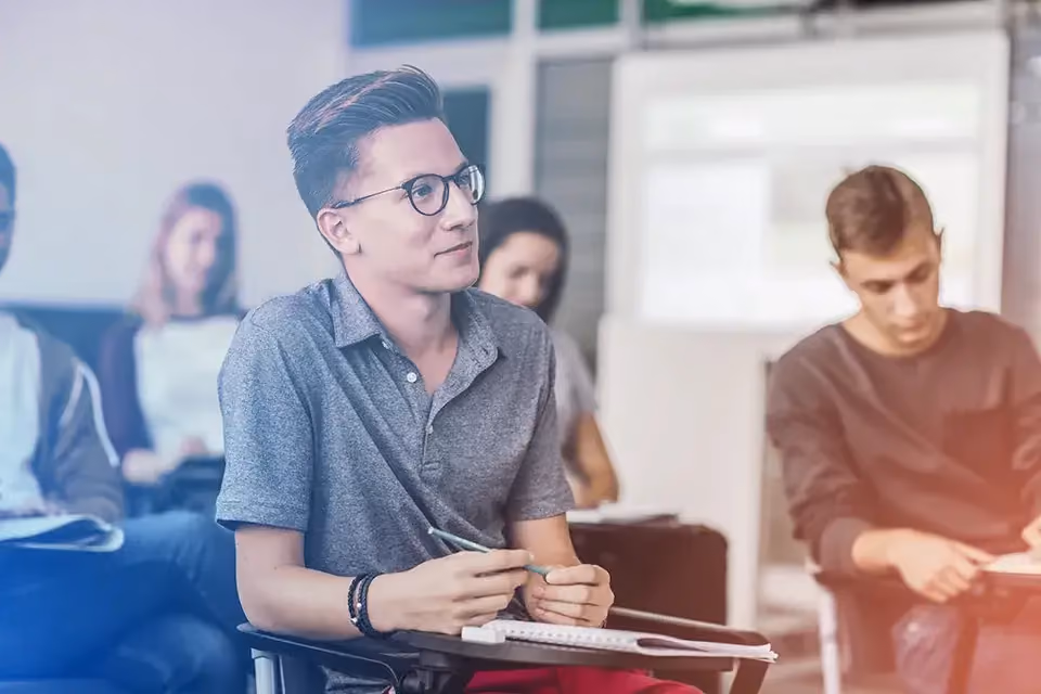 Jeune homme à lunettes souriant, en classe parmi d'autres élèves