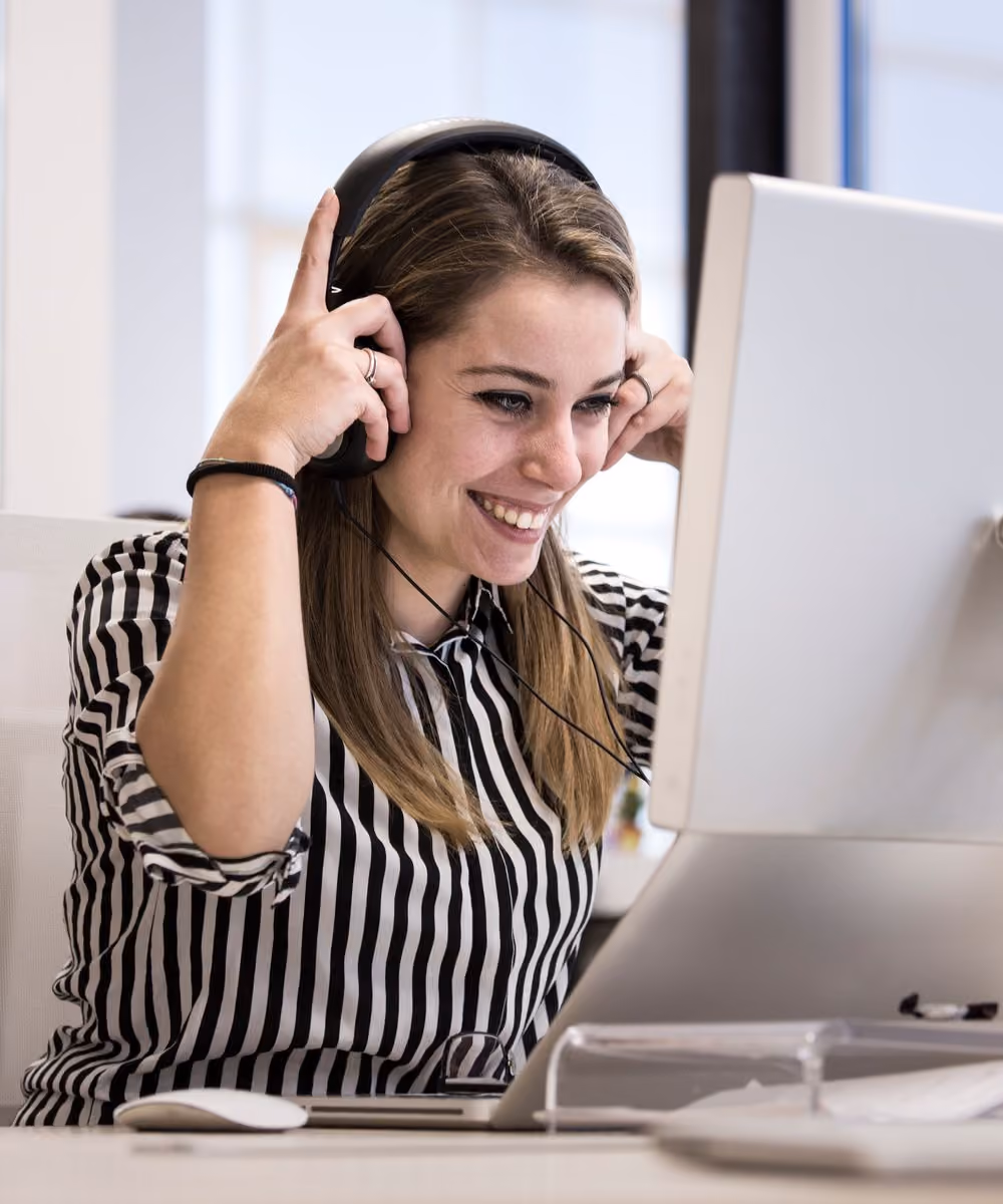 Business developer souriante, casque audio, devant son écran