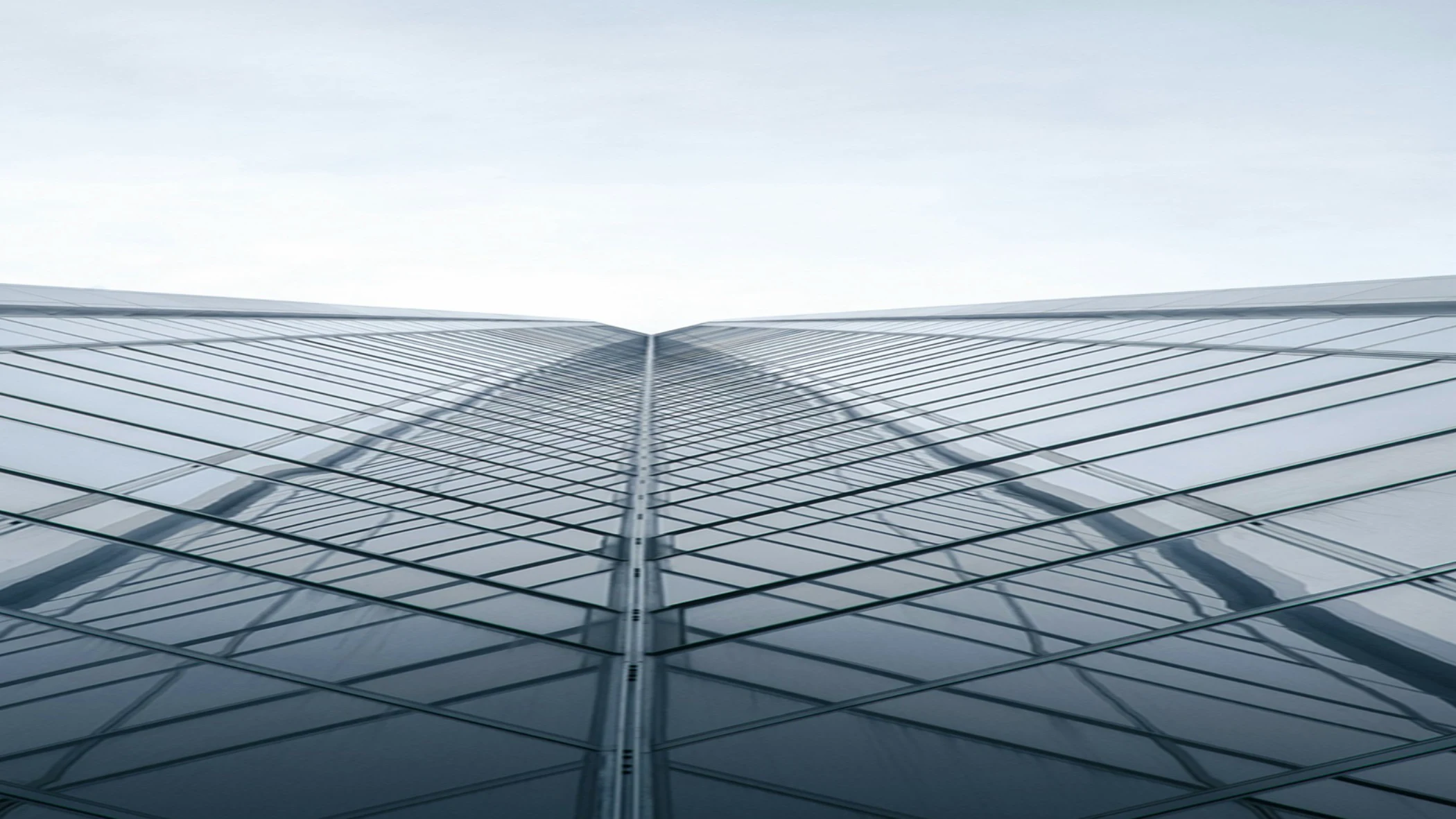 Upward view of a modern glass skyscraper with reflective windows and geometric lines.