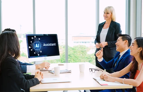 Three colleagues in a conference room having a video call with five people shown on a large screen.
