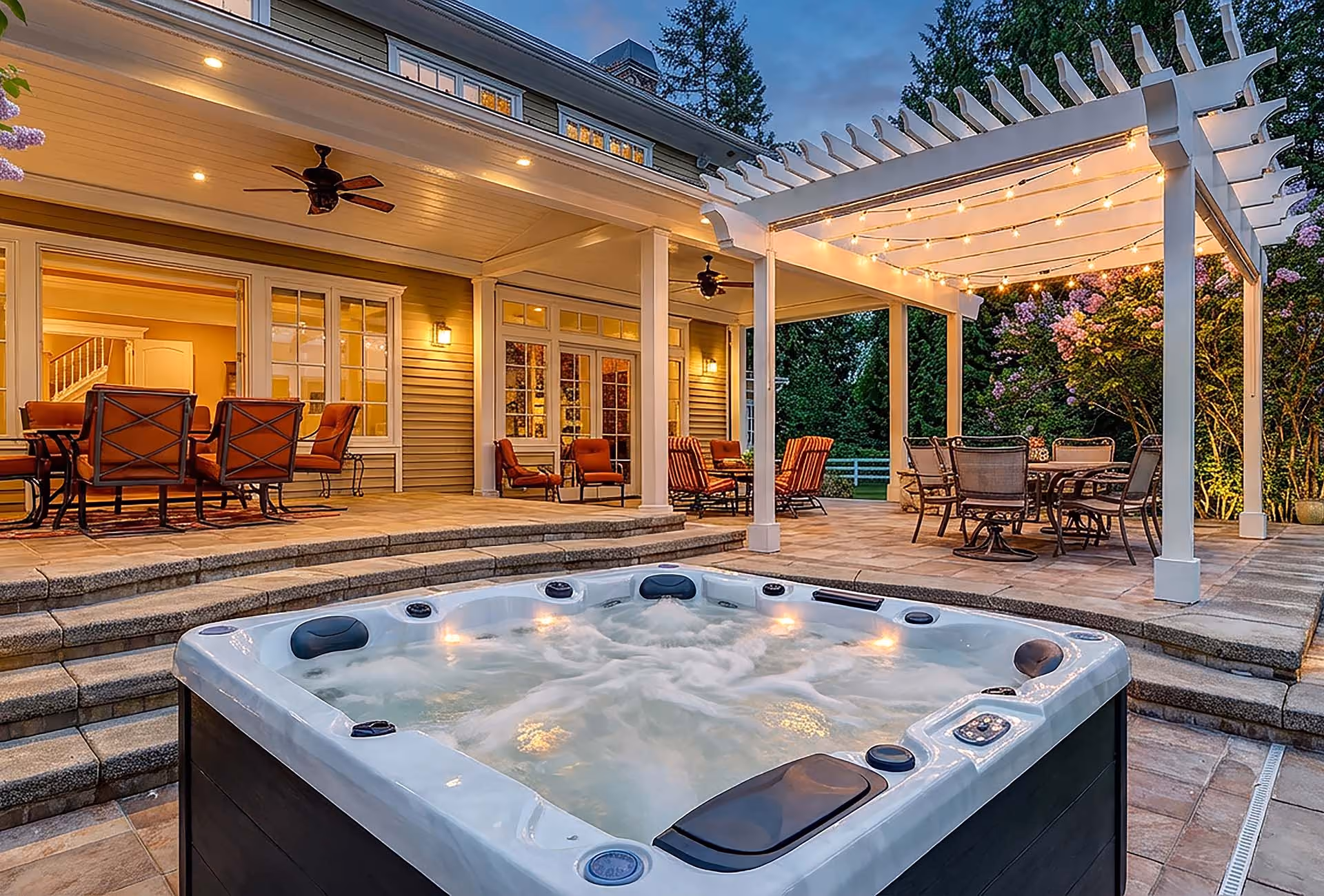 Outdoor patio with a hot tub, seating areas, pergola with string lights, and a house in the background.