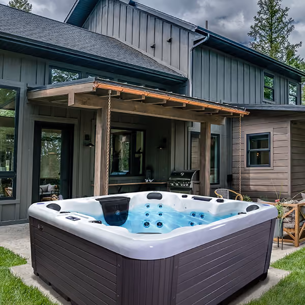 Outdoor hot tub with clear water in front of a modern gray house under a wooden pergola.