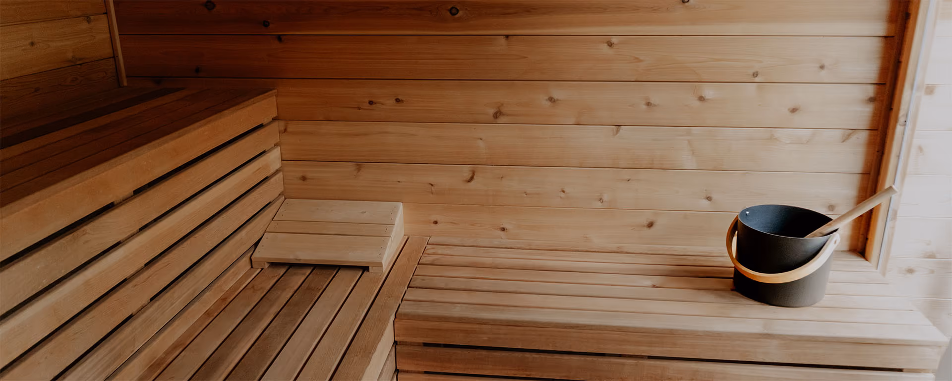 Interior of a wooden sauna with a black bucket and ladle resting on a bench.