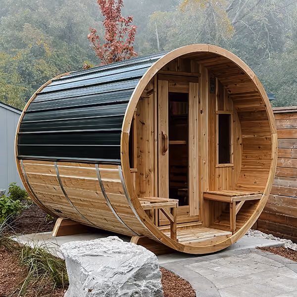 Round wooden outdoor sauna with door, window, and benches on a stone patio surrounded by trees.