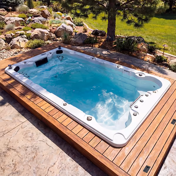 Rectangular swim spa with clear blue water surrounded by wooden deck and garden landscaping.