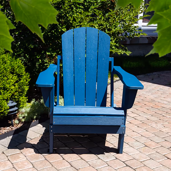Blue Adirondack chair on a stone patio surrounded by green bushes and leaves.