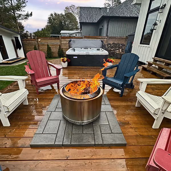 Outdoor wooden deck with fire pit surrounded by Adirondack chairs and a hot tub in the background.