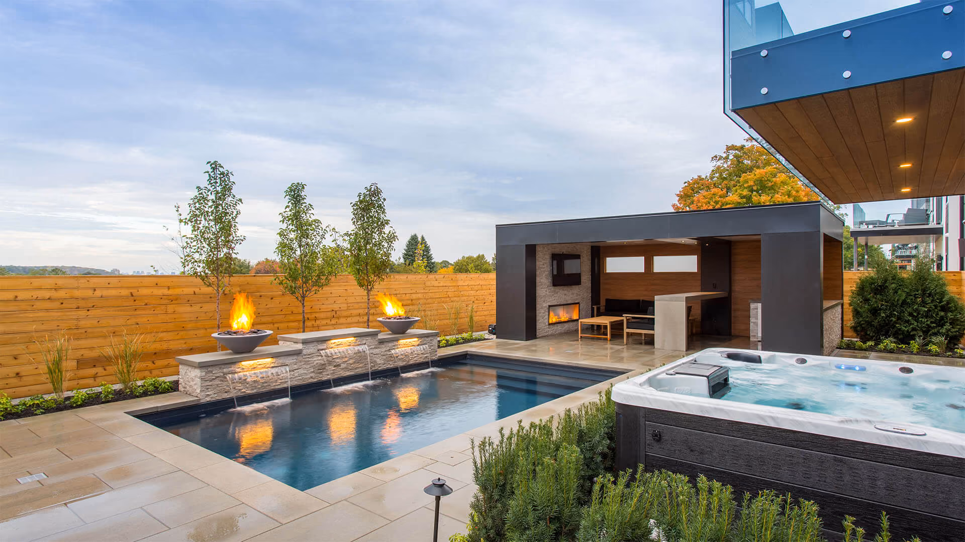 Modern backyard with pool, hot tub, fire features, and covered patio with seating and fireplace.