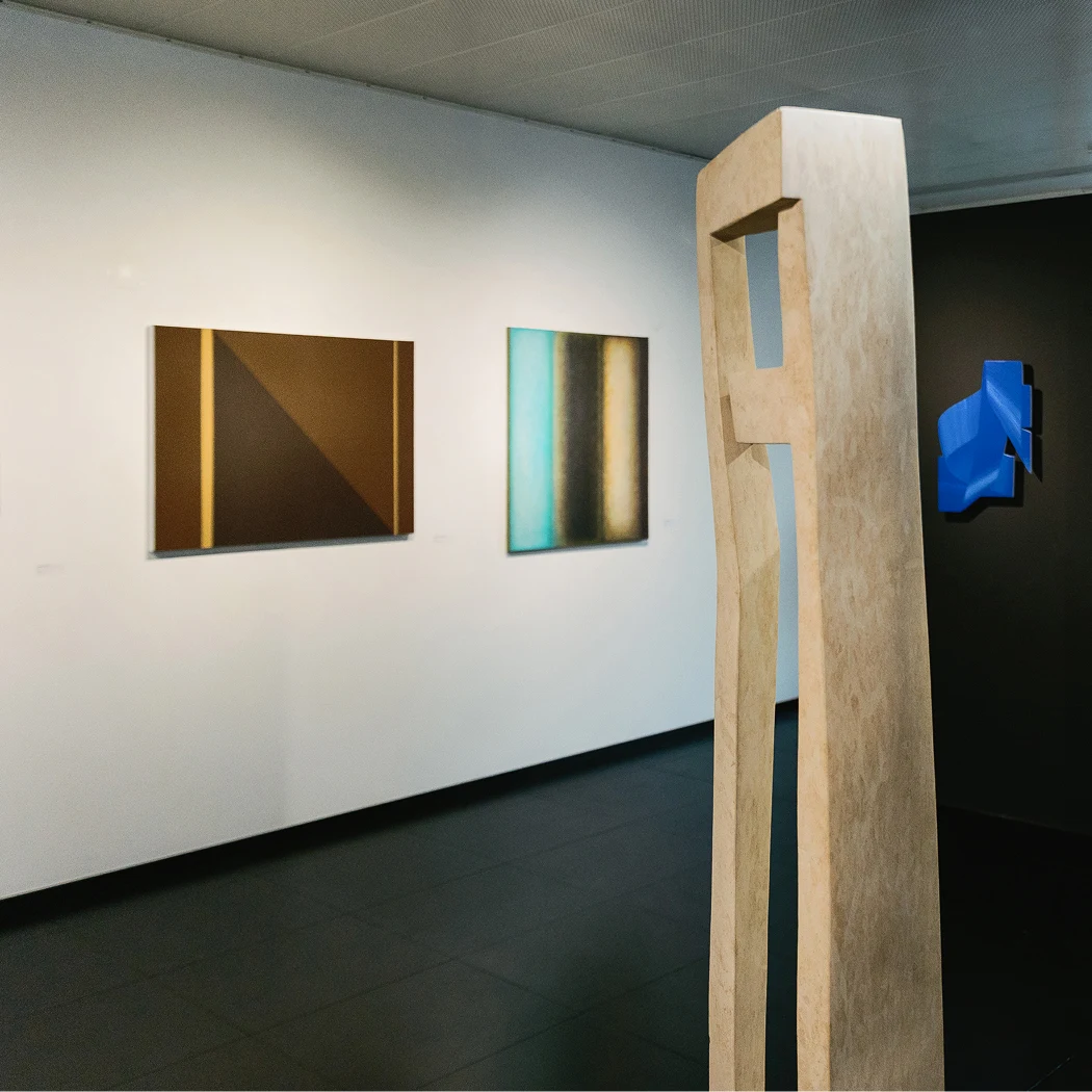Sala della galleria d’arte contemporanea Lugano con scultura in legno e dipinti astratti.