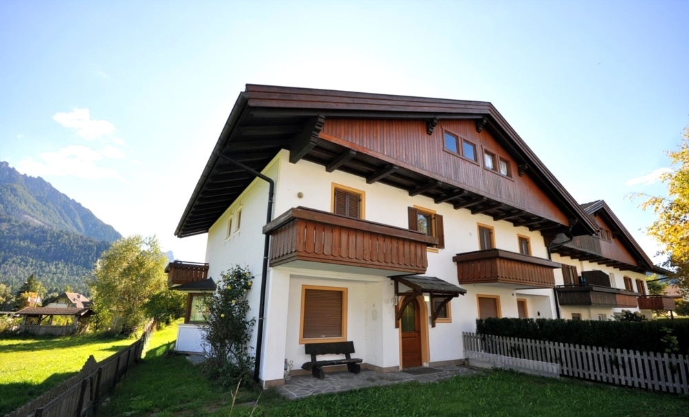 White multi-unit chalet with wooden balconies and mountain view under clear blue sky.