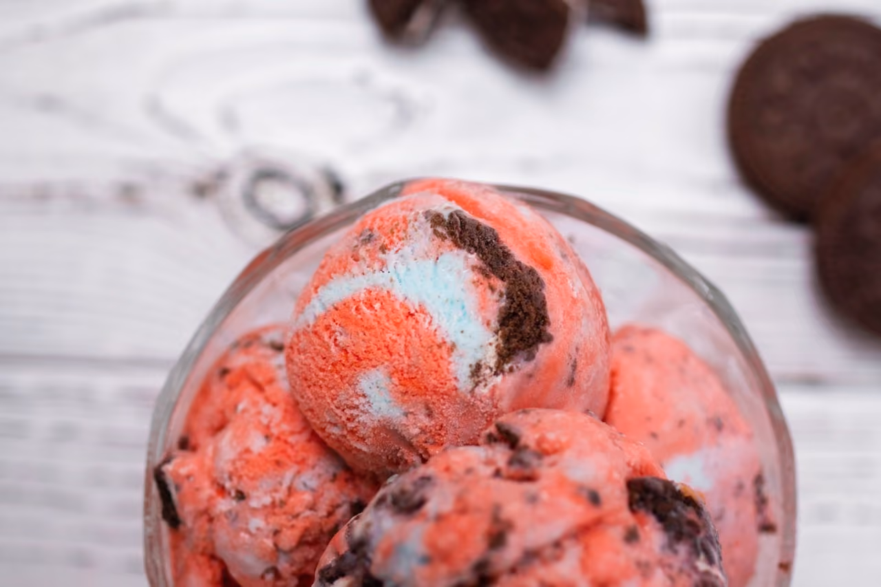 Scoops of red and white ice cream with chocolate cookie pieces in a glass bowl.