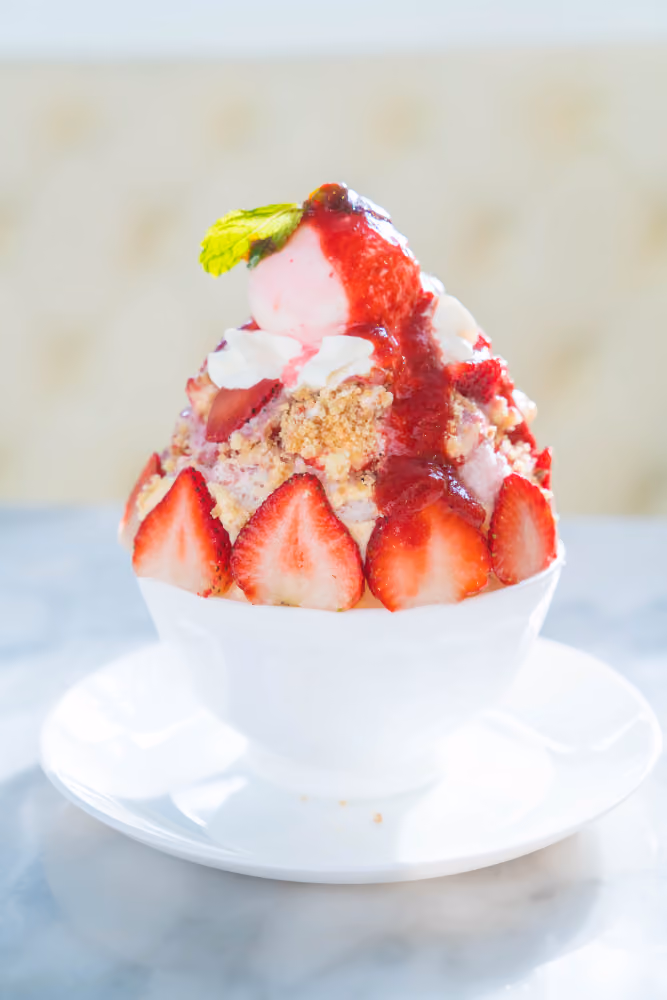 Bowl of strawberry dessert with sliced strawberries, crumb topping, whipped cream, and mint leaf on top.