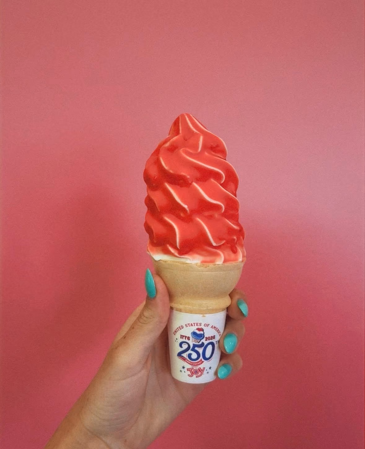 Hand with turquoise nails holding a soft serve ice cream cone with red and white swirled ice cream.