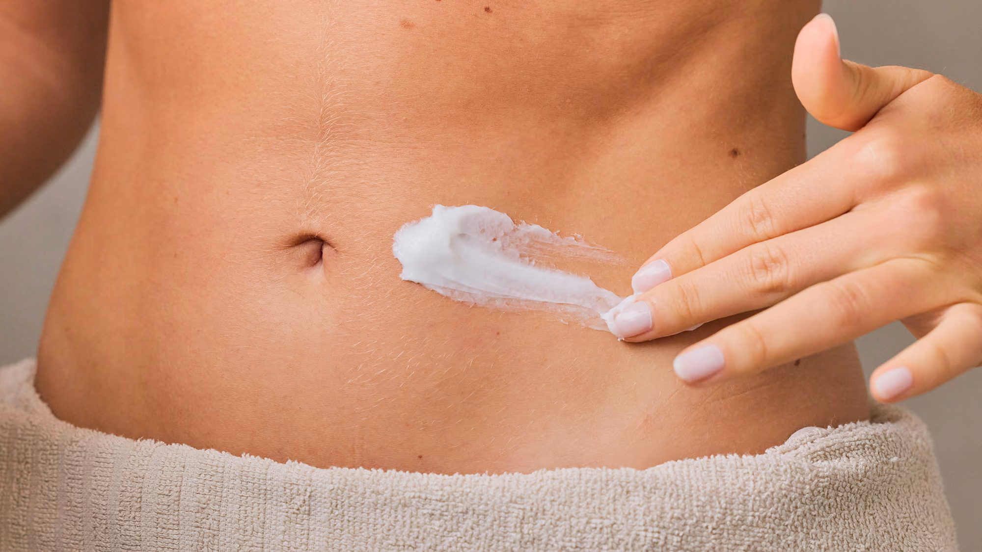Woman putting skin cream on her abdomen.