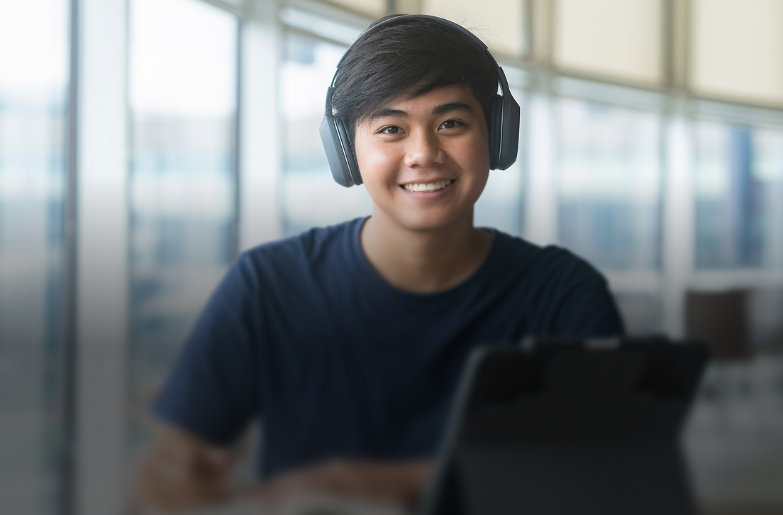 Smiling young man with headphones in front of a tablet, sitting in a bright modern room.