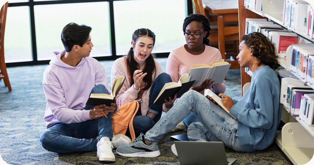 Four students sitting on a library floor reading and talking