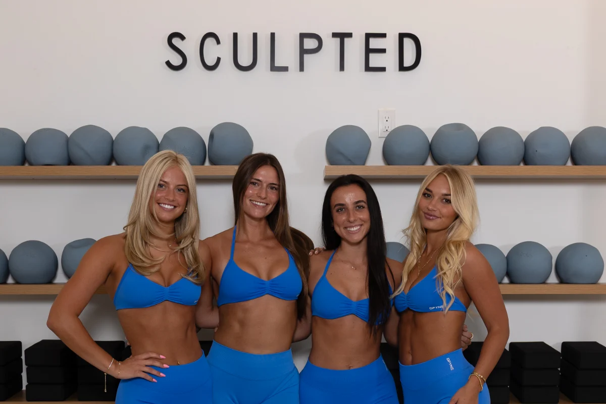 Four smiling Sculpted instructors in matching blue sets in front of the Sculpted wall