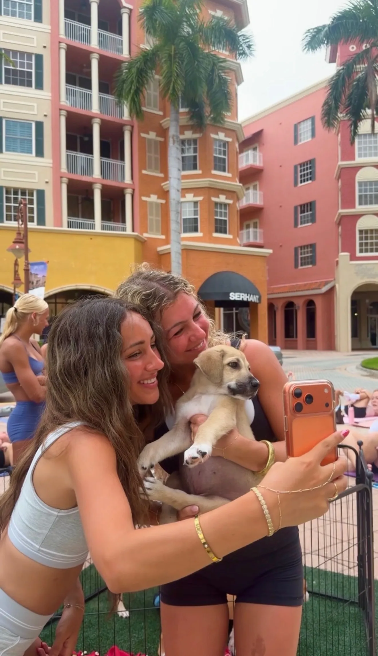 Two members holding an adoptable puppy at Puppy Pilates outside at Bayfront Place, Naples