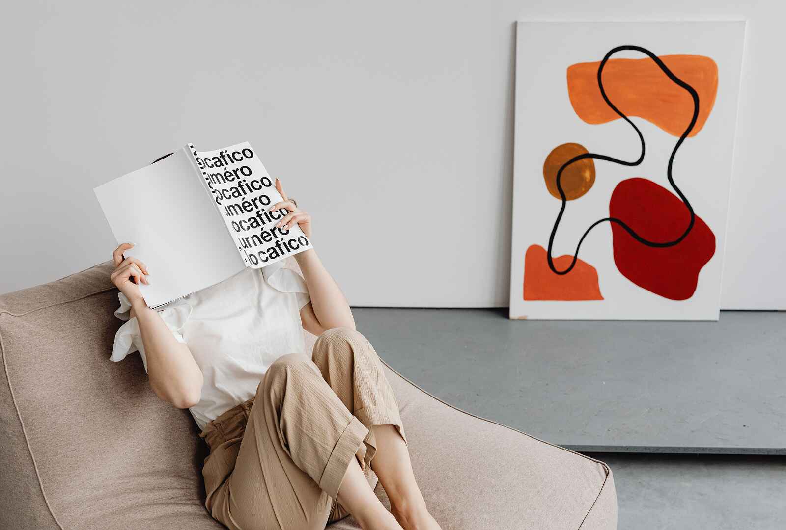 A girl reading a red book while sitting on a sofa.