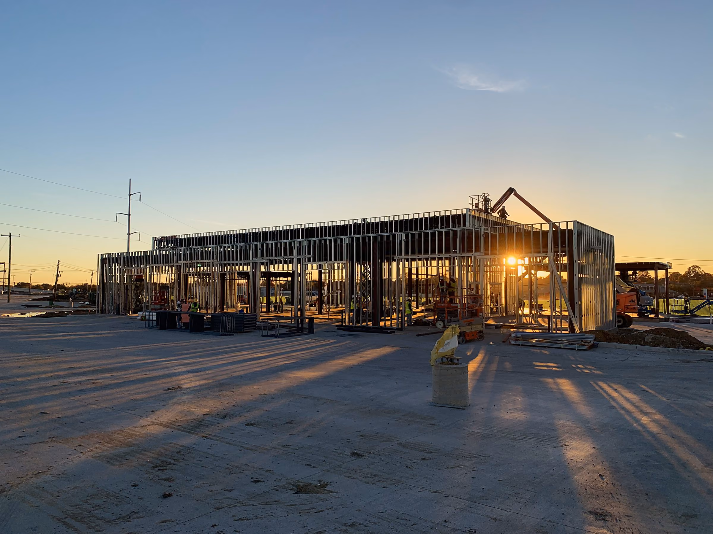 Crane setting a steel truss at sunset on a commercial jobsite near Plano, Texas