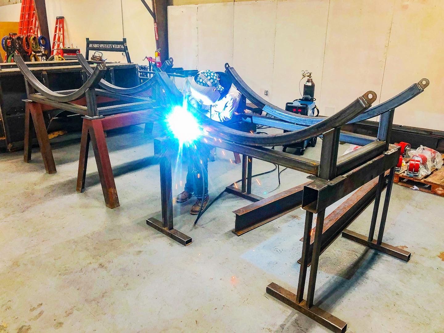Welder fabricating a curved-arm steel cradle frame on sawhorse stands in the shop