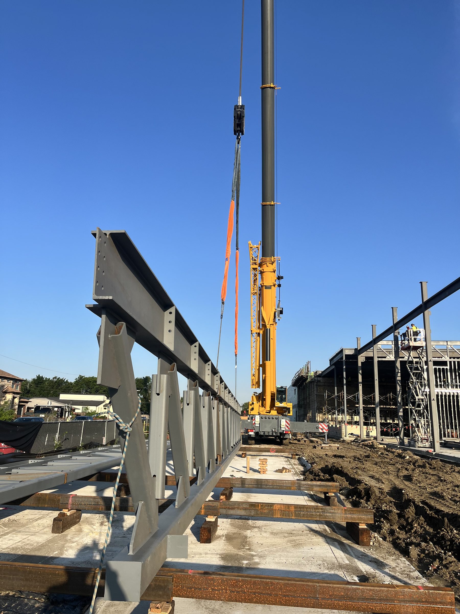 Fabricated steel girders staged on cribbing beside a mobile crane ready for the lift