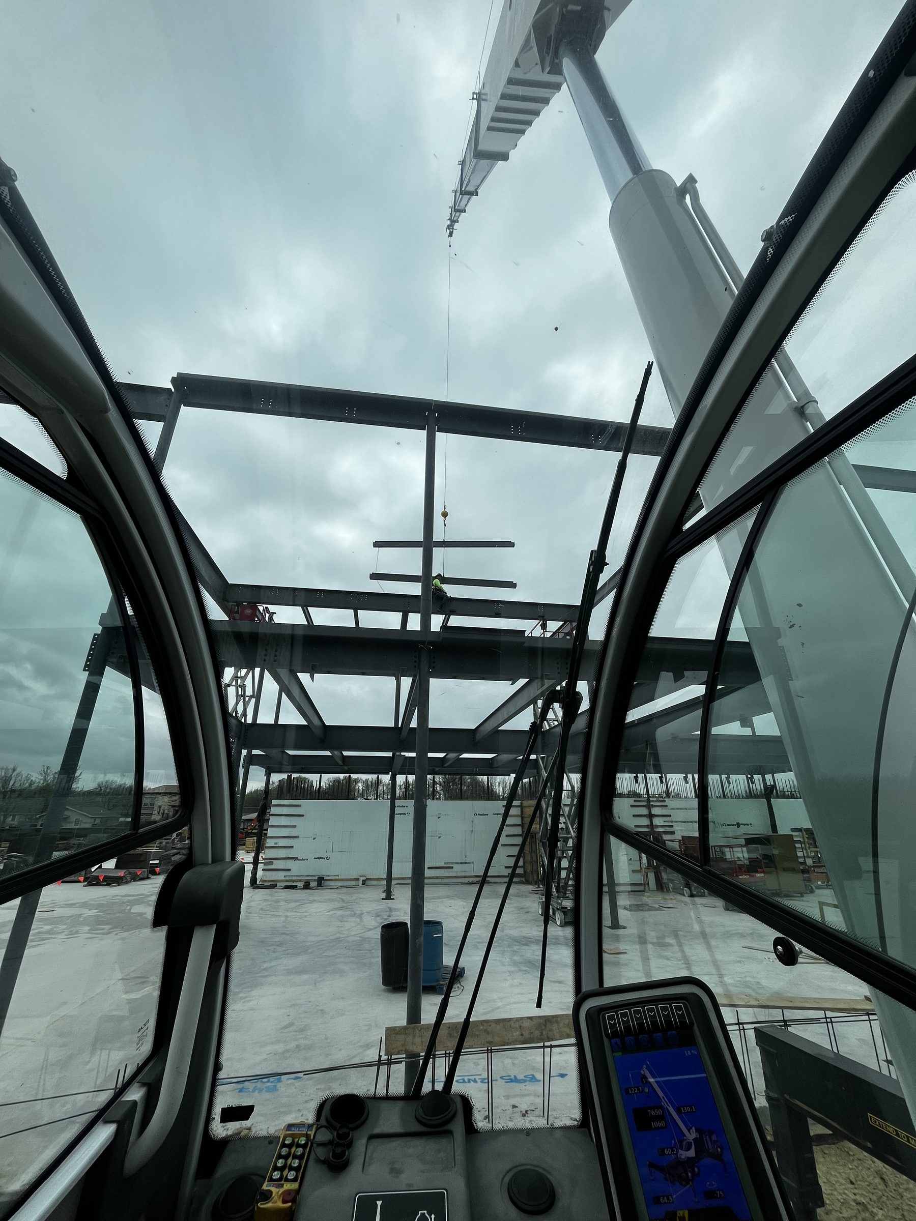 View through the crane operator's cab windows looking up at a steel member on the hook