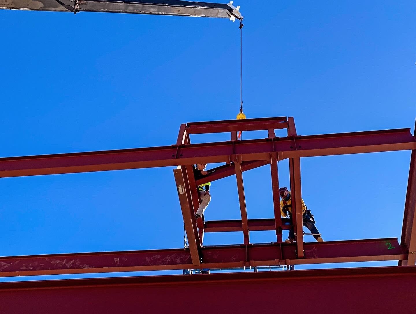 Ironworkers connecting a crane-lifted steel assembly on a dealership frame