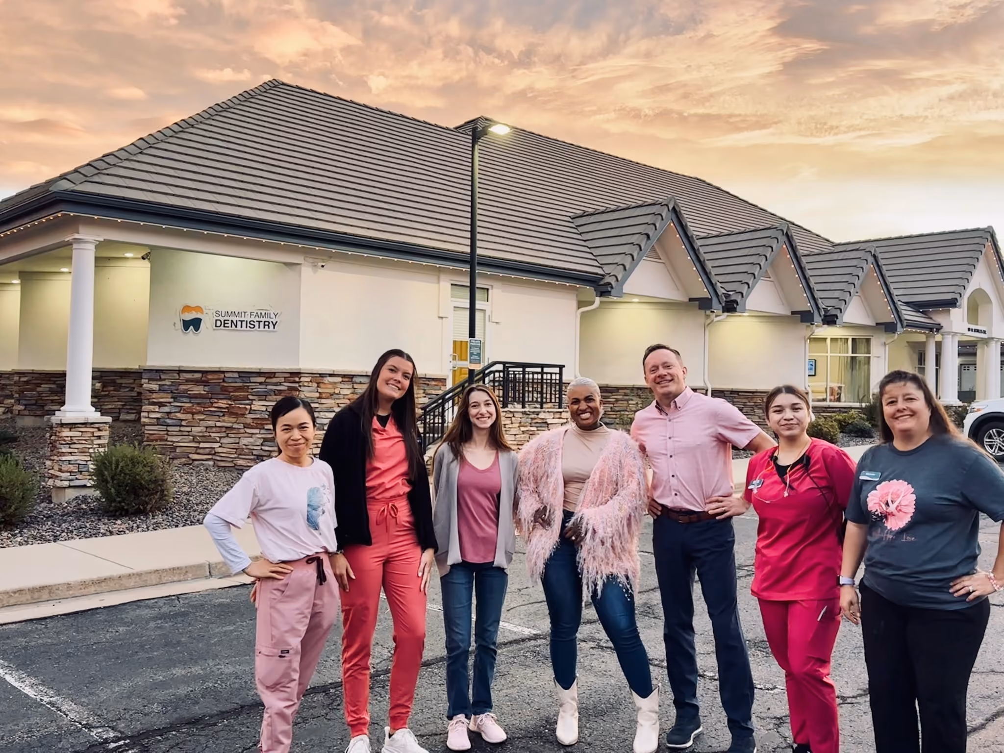 Group of smiling dental office staff standing outside Summit Family Dentistry at sunset.