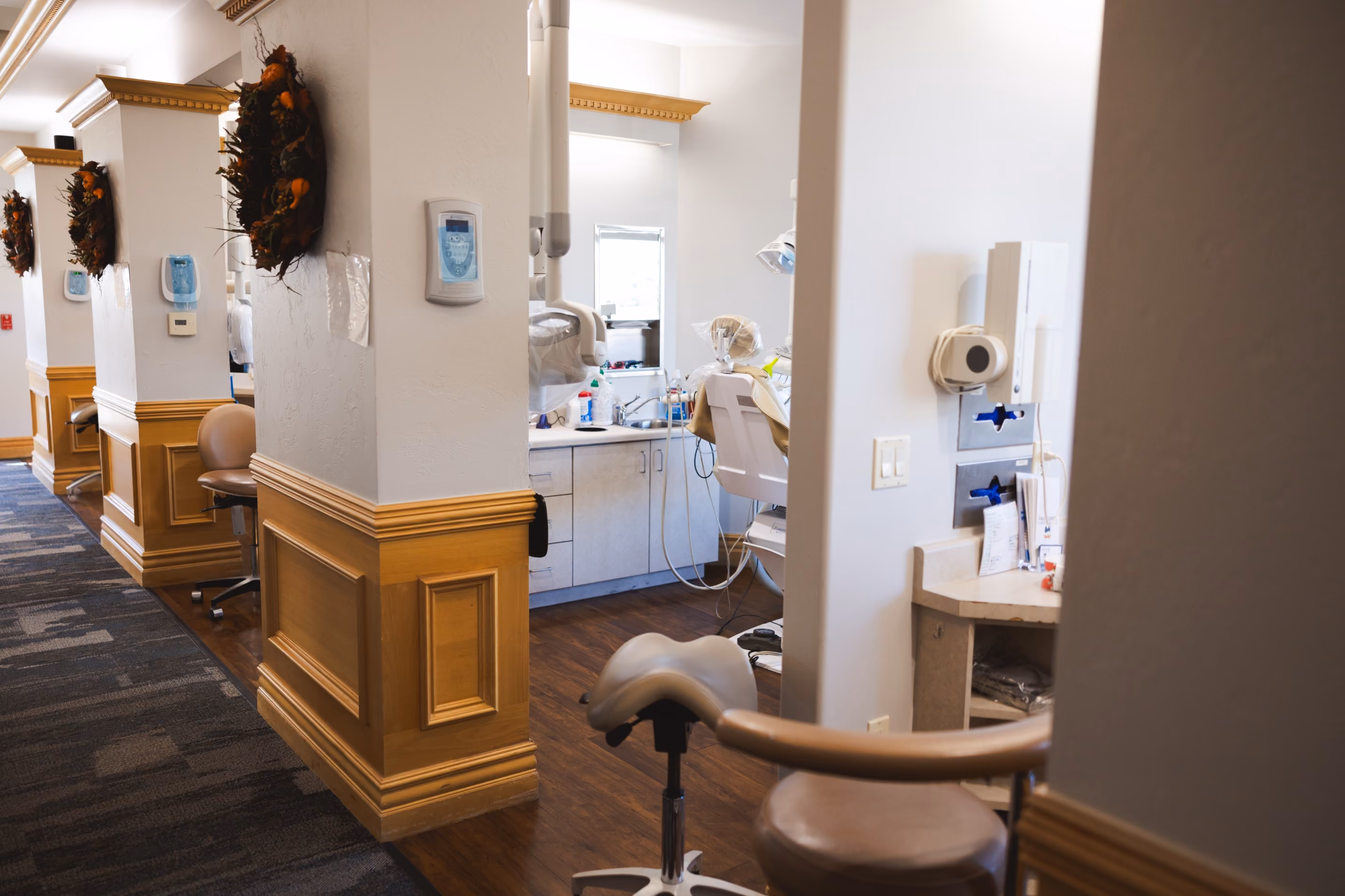 Hallway with dental office stations featuring chairs, dental equipment, and autumn wreaths on columns.