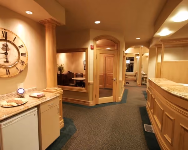 Warm-toned hallway with wooden trim, a large clock, and a countertop with plates and snacks.