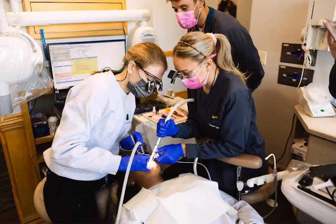 Dental professionals wearing masks and gloves treating a patient in a dental clinic.