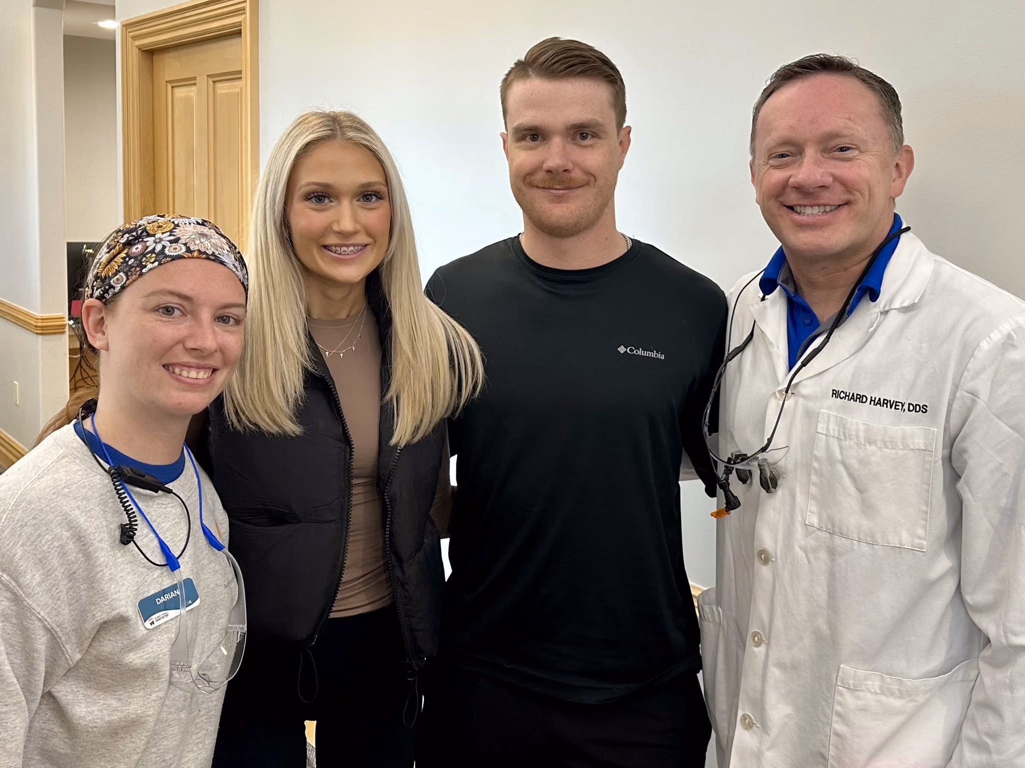 Smiling group of four people, including a man in a dentist coat labeled Richard Harvey, DDS.