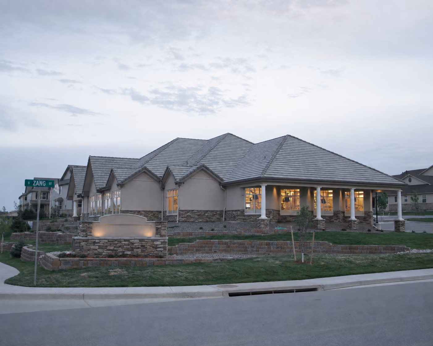Single-story building with stone foundation and lit windows at dusk on a corner lot near Zang Street.
