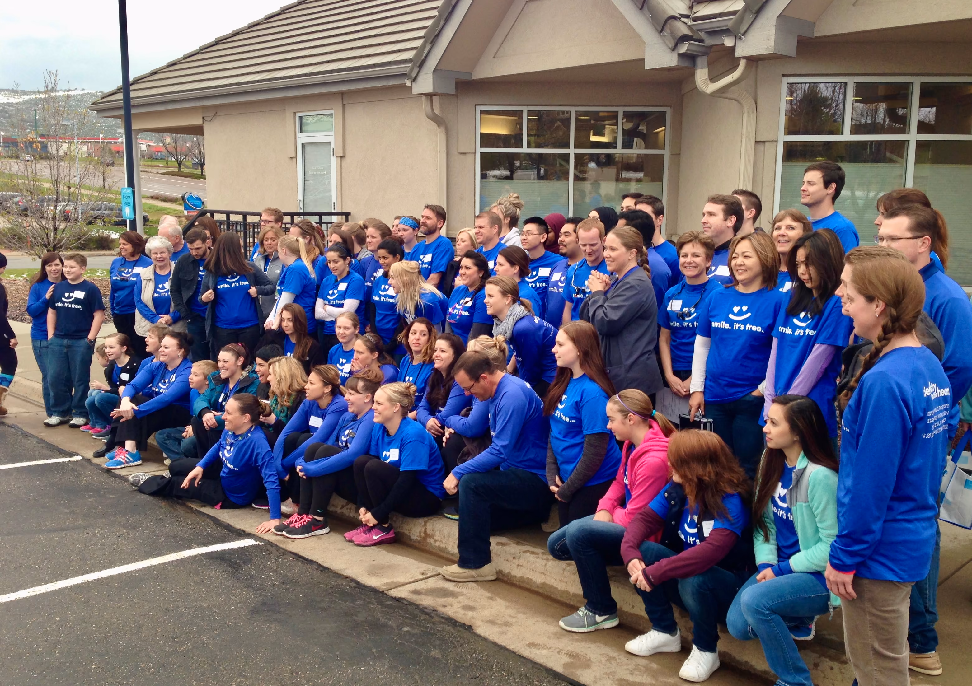 Large group of people in blue shirts posing outside a building for a group photo.