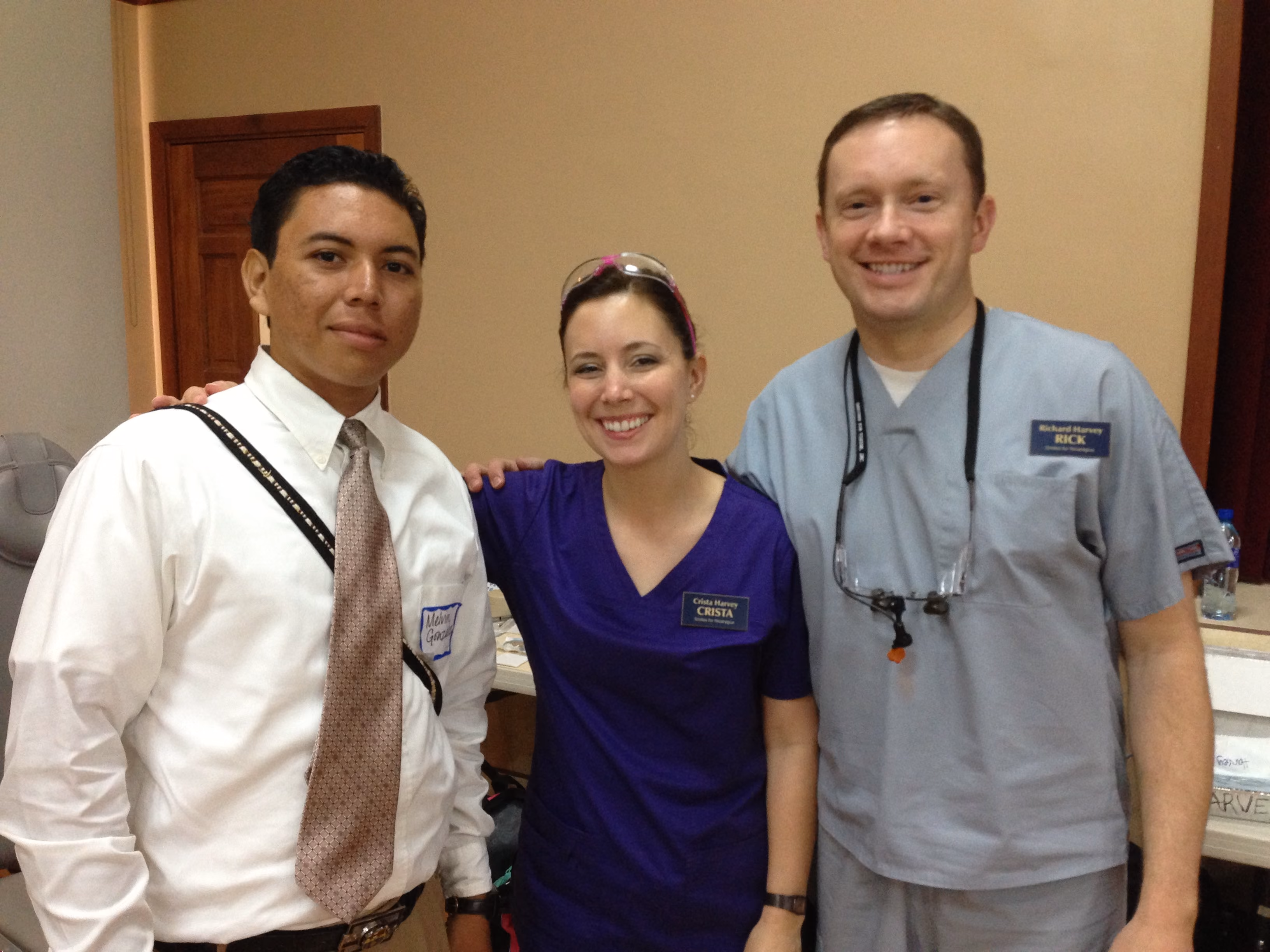 Three smiling medical professionals with name tags posing indoors in casual and scrubs attire.