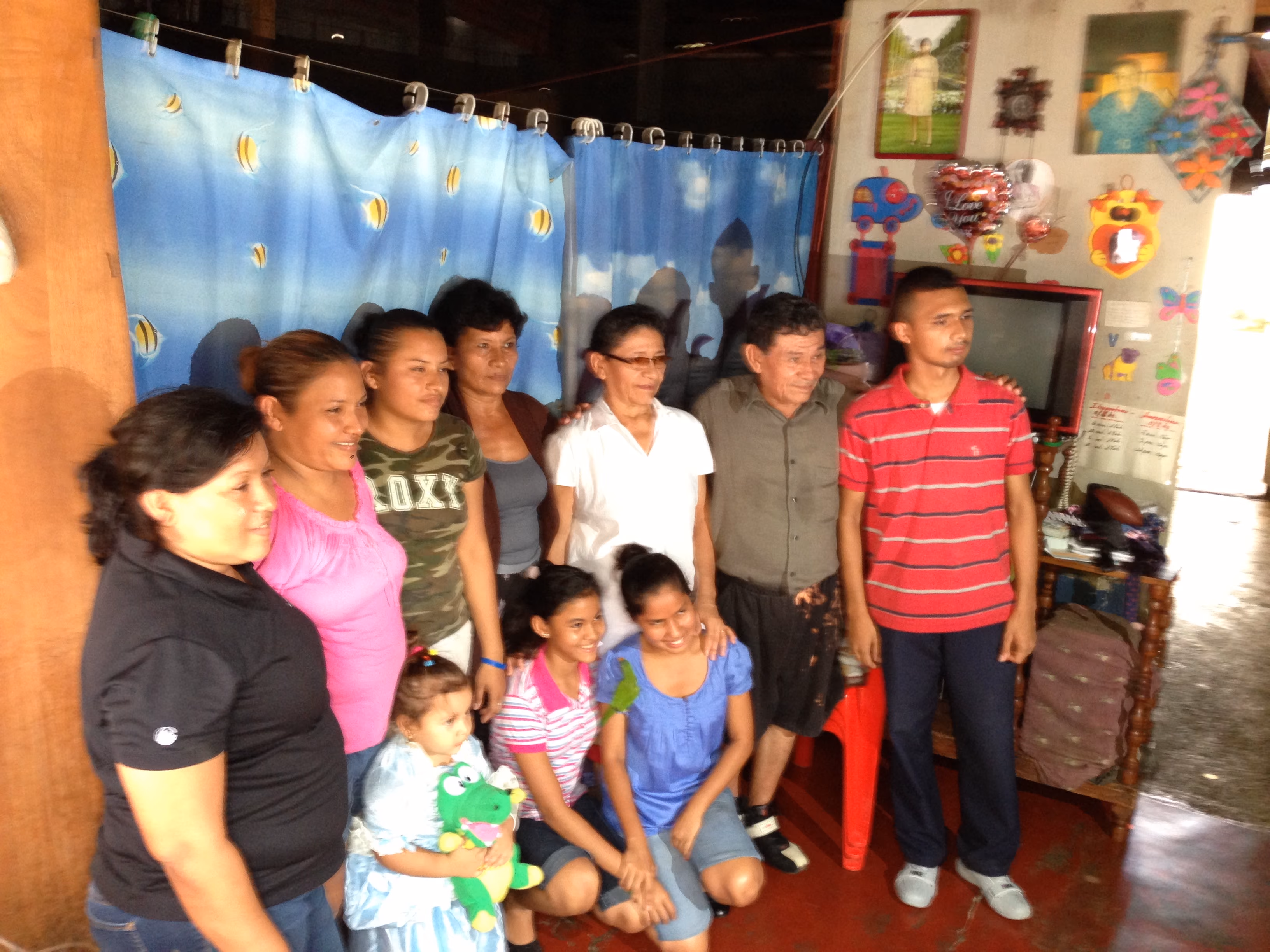 Group of nine people, including children and adults, posing inside a decorated room with blue curtains.