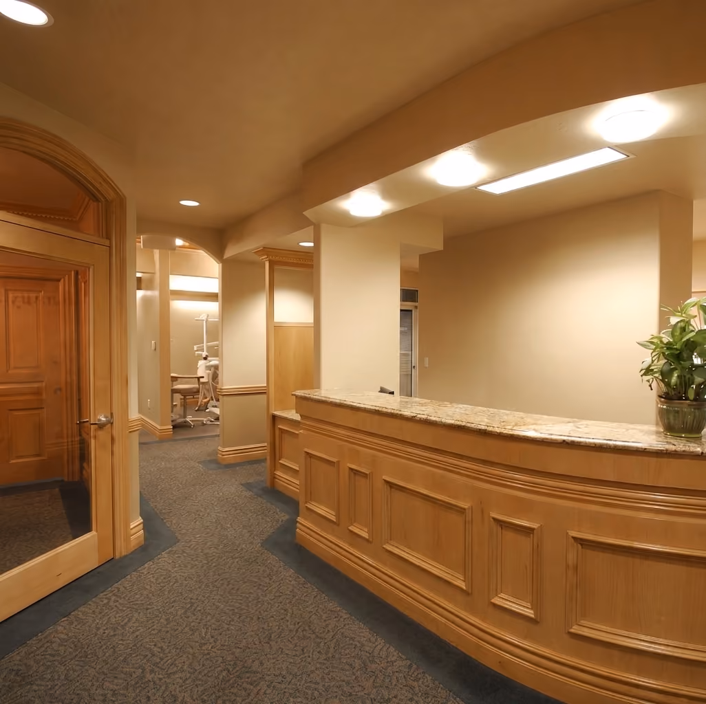 Dental office reception with wood-paneled desk, carpeted floor, and a plant on the counter.