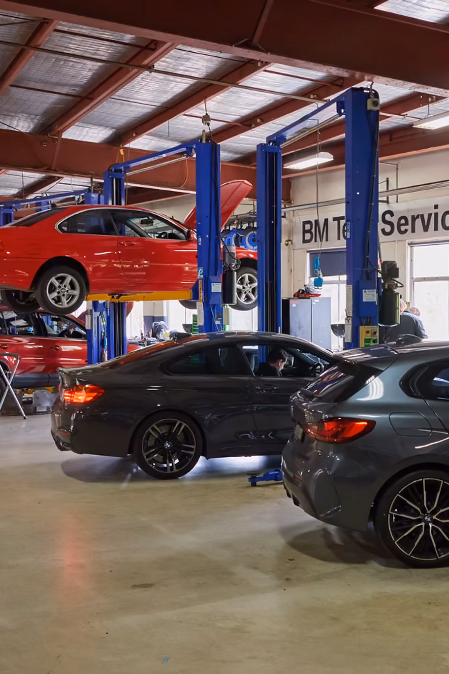 Wide view of a car repair shop with several cars being serviced on lifts and on the ground.