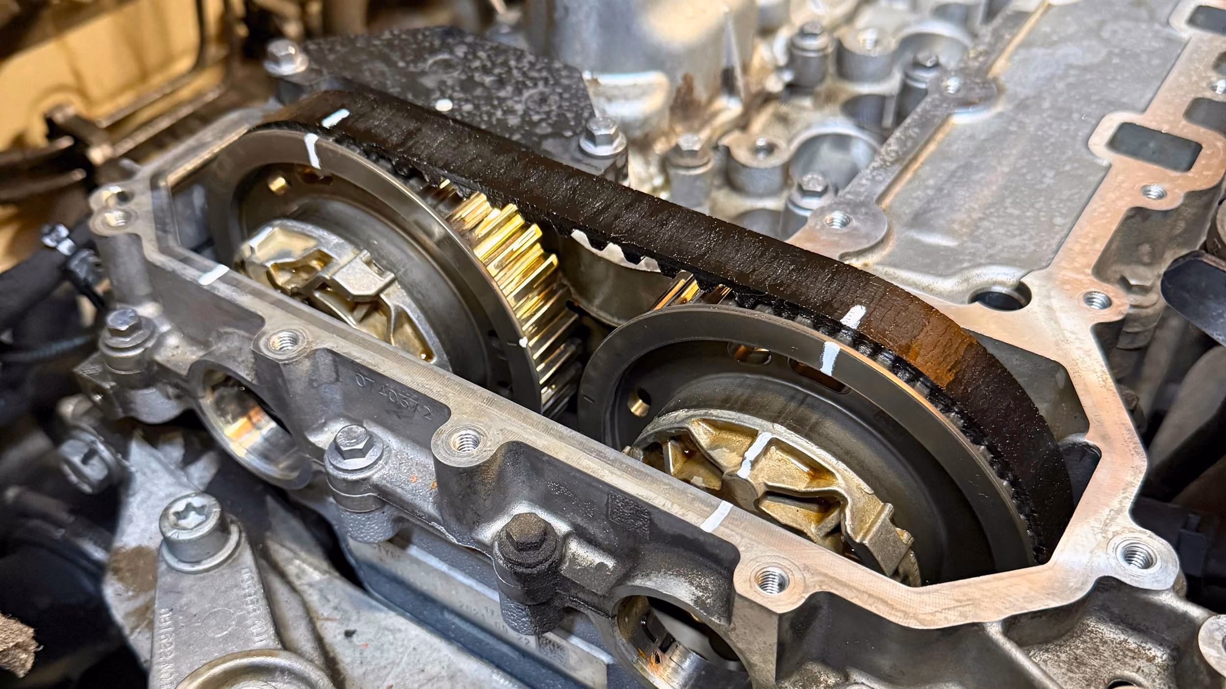 Close-up of a wet timing belt and camshaft sprockets with white alignment marks on the engine block.