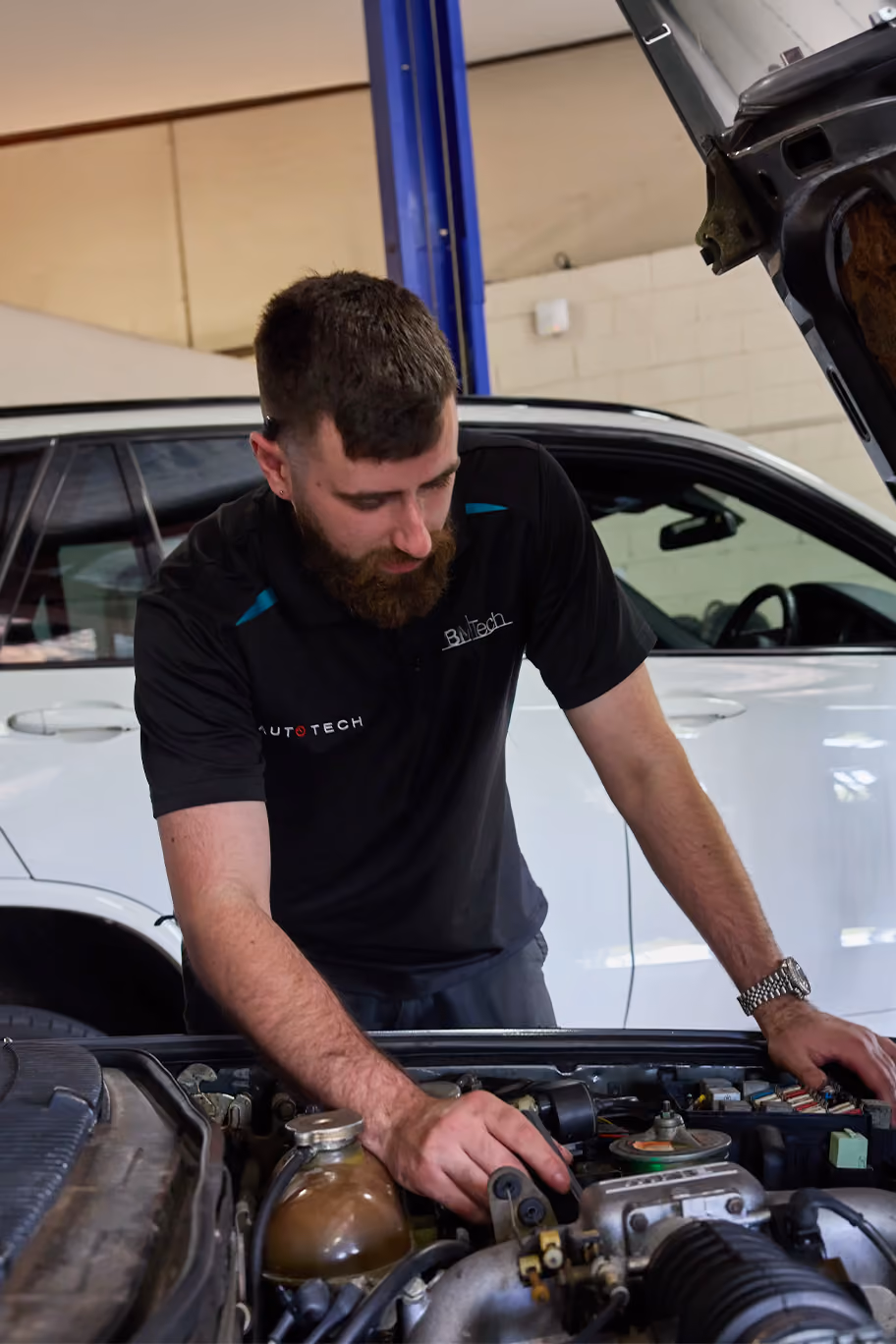 Mechanics working on a white Mercedes SUV in a busy Melbourne workshop during a car inspection.
