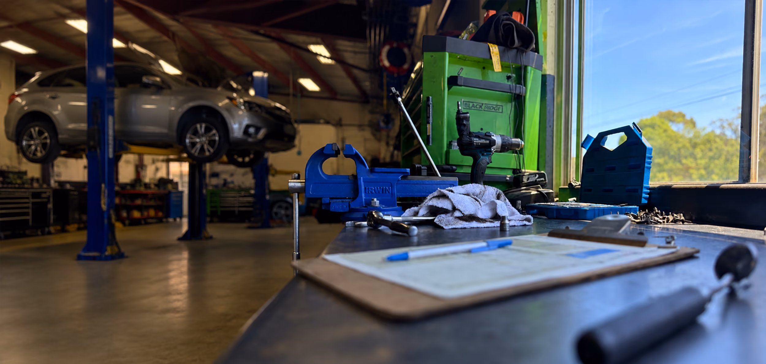 Roadworthy inspection checklist and tools on a workshop bench with a vehicle on a hoist in the background.