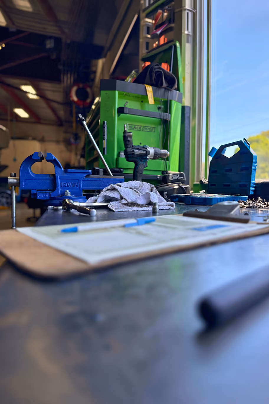 Roadworthy inspection checklist and tools on a workshop bench with a vehicle on a hoist in the background.