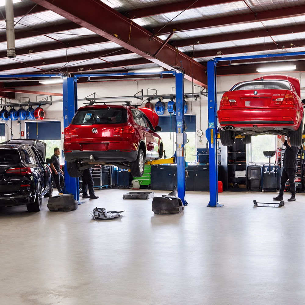 BMW and Volkswagen vehicles on hoists inside the BM Tech workshop, with technicians carrying out servicing and repairs.